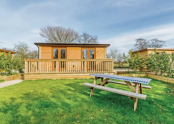 A wooden cabin with a deck, a picnic table, and a grassy yard. - Compact lodge finished to a high standard with one double and one with bunks. (Pickering)