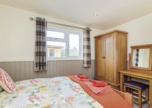 Une chambre à coucher avec un lit, une fenêtre avec des rideaux, une armoire en bois et une petite table avec une chaise.