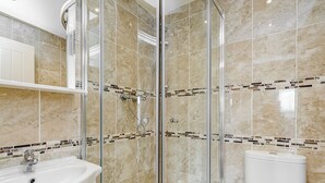 Un baño con ducha envuelta en vidrio, lavamanos e inodoro.