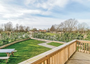 Um deck de madeira com vista para um jardim bem cuidado e uma casa ao fundo.