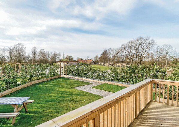 Une terrasse en bois offrant une vue sur un jardin bien entretenu et une maison en arrière-plan.
