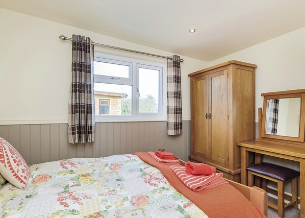 Une chambre à coucher avec un lit, une fenêtre avec des rideaux, une armoire en bois et une petite table avec une chaise.