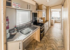 Cocina compacta con lavamanos, estufa y armarios. Se observa un cartel de 'No Smoking'.