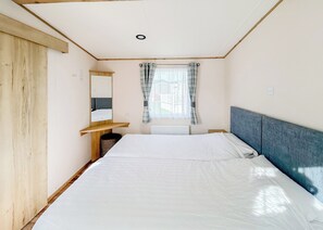 Una habitación con cama, cabecero de madera, espejo, ventana con cortinas y radiador.