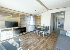 Una sala de estar moderna con un televisor de pantalla plana, estanterías de madera, una mesa de comedor con sillas y un sofá gris.