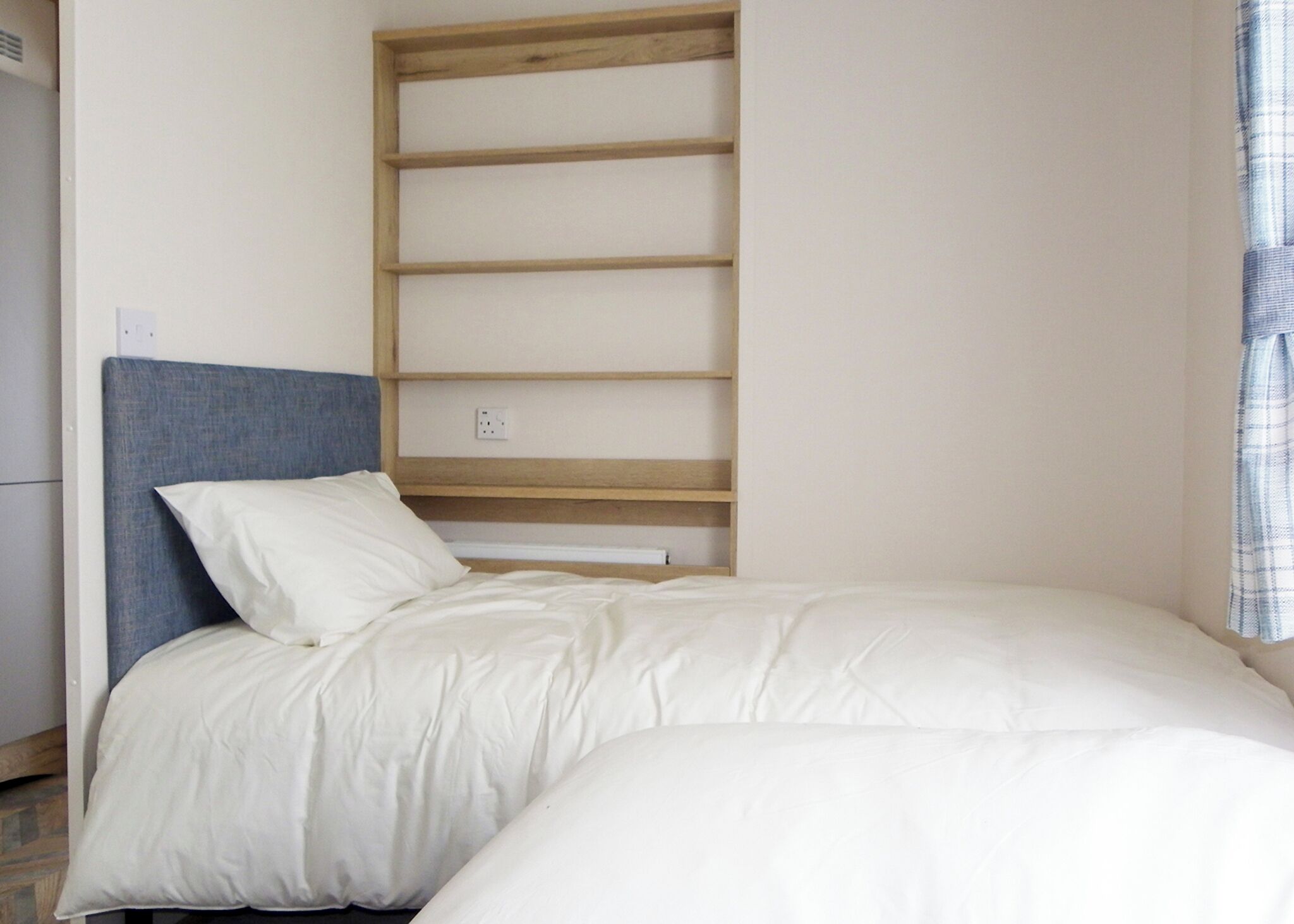 Une chambre à coucher comprenant un lit, une tête de lit, une étagère en bois et une prise de courant.