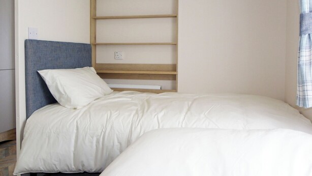 Ein Schlafzimmer mit einem Bett, einem Kopfteil, einer Holzregaleinheit und einer Steckdose.