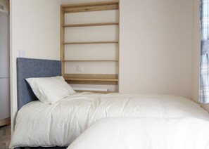Un dormitorio con cama, cabecera, estantería de madera y toma de corriente.