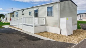 Ein eingeschossiges Mobilheim mit eingezäunter Terrasse, einer kleinen Veranda und einer Garage.