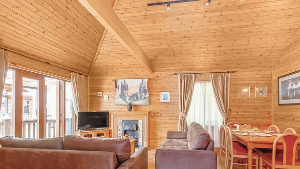 Interior de una cabaña de madera con sala de estar, mesa de comedor y chimenea.