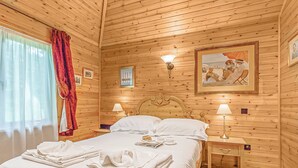 Una habitación de madera con una cama, dos lámparas de noche, una mesita de noche y un cuadro en la pared.