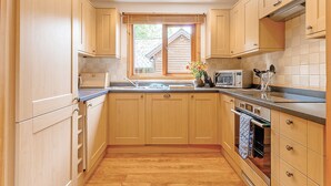 Una cocina con armarios de madera, microondas y ventana con persianas.
