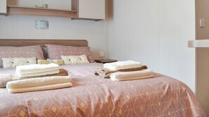 A bedroom with a bed, pillows, a nightstand, and a wall-mounted shelf.