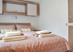 A bedroom with a bed, pillows, a nightstand, and a wall-mounted shelf.