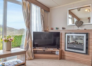 Uma sala de estar moderna com televisão de tela plana, lareira, janelas amplas com cortinas e vista para o exterior.