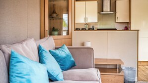 Ein modernes Wohnzimmer mit einer Couch, blauen Kissen, einem kleinen Tisch und einer Küchenzeile mit Schränken und einem Herd.
