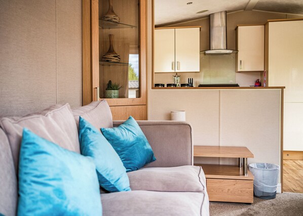A modern living room with a sofa, blue cushions, a small table, and a kitchen area with cabinets and a stove.