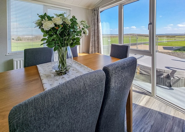 A dining area with a table, chairs, a vase with flowers, and a view through large windows.