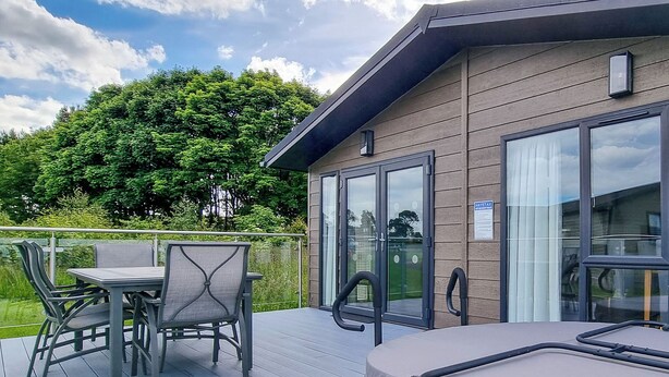 A deck with a table and chairs, a hot tub, and a glass door leading to a room. - Chestnut Lodge (P/F) VIP (Knitsley)