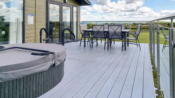 Una terraza con jacuzzi, mobiliario exterior y un ventanal que da a una zona cubierta.
