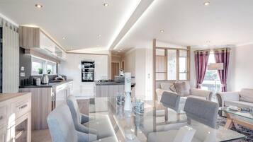 A modern kitchen with built-in appliances, a dining area with a glass table, and a living room with a sofa and a coffee table.