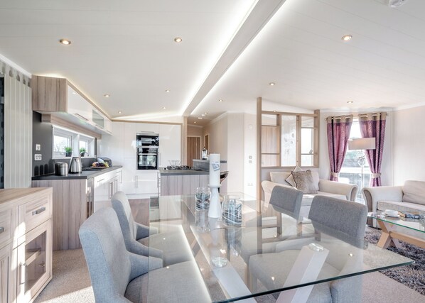 Eine moderne Küche mit Einbaugeräten, ein Essbereich mit Glastisch und ein Wohnzimmer mit Sofa und Couchtisch.