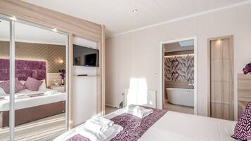A modern hotel room with a large bed, a TV, a bathroom with a bathtub, and a sliding glass door.