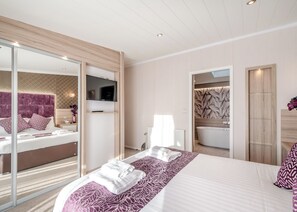 Ein modernes Hotelzimmer mit einem großen Bett, einem Fernseher, einem Badezimmer mit Badewanne und einer Schiebeglastür.