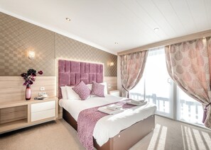 A bedroom with a large bed, bedside tables, a vase with flowers, and a window with curtains.