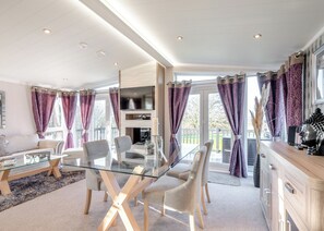 Ein modernes Wohnzimmer mit einem Glastisch, bequemen Sitzgelegenheiten, einem Flachbildfernseher und Blick ins Freie.