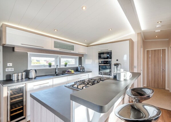 A modern kitchen with a central island, built-in appliances, and a view to the outdoors. - Criffel Hilltop Lodge (Dumfries, Dumfries & Galloway)