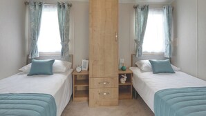 Une chambre avec deux lits, une armoire en bois, une table de chevet et une fenêtre avec des rideaux.