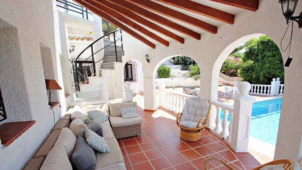 Un espacio de estar al aire libre techado con sofá, sillas y vista a una piscina.