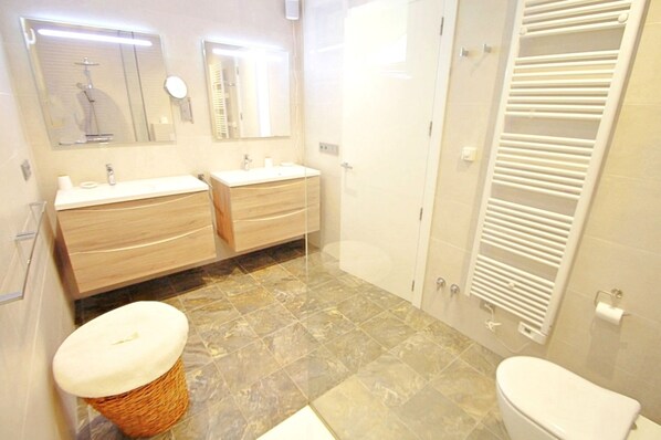 A bathroom with two sinks, a toilet, a mirror, and a towel rack.