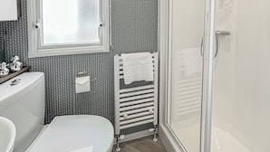 Et badeværelse med toilet, vask, bruseniche med glasdør og en radiator.