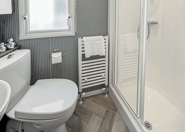 A bathroom with a toilet, a sink, a shower with a glass door, and a radiator. - Contemporary caravan with one double and one twin. (LLwyngwril, Gwynedd)