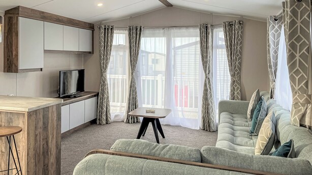 En moderne stue med sofa, fjernsyn, et lille bord og en balkon med gardiner.