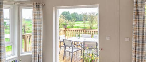 Una habitación con un ventanal grande, una terraza de madera y vistas a un paisaje verde.