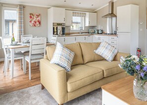 A modern kitchen with white cabinets, a beige sofa, and a dining area with white chairs.