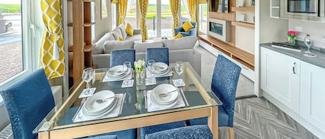 Un área de comedor con una mesa de vidrio, sillas azules y un sofá al fondo.