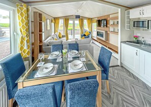 A dining area with a glass table, blue chairs, and a sofa in the background.
