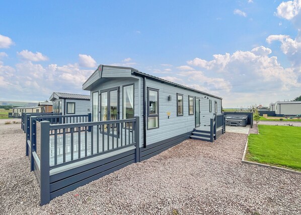 A mobile home with a deck, large windows, and a gravel driveway.