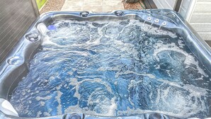 Ett bubbelbad med flera massagemunstycken, omgivet av ett trädäck och en mur av tegelsten.