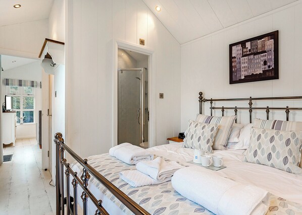 Een slaapkamer met een bed, kussens, een nachtkastje, een wandafbeelding en een douchegedeelte.