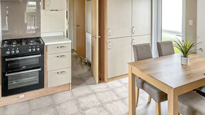 Una cocina con estufa, horno, alacenas y una mesa de comedor con sillas.