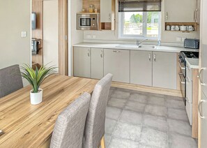 A modern kitchen with a wooden dining table, grey chairs, and a potted plant. - 2 bedroom accommodation in Laurenkirk (Laurenkirk)
