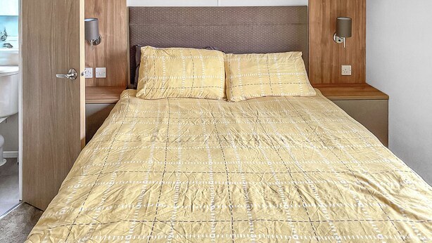 Una cama bien hecha con una colcha estampada, un cabecero de madera y lámparas de noche.