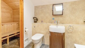 Un baño con un banco de madera, un inodoro, un lavamanos y un espejo.