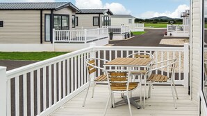 Een terras met buitenmeubilair, witte relingen en uitzicht op stacaravans.