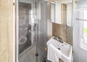 Ein modernes Badezimmer mit Duschkabine aus Glas, einem weißen Waschbecken mit Holzschrank und einem Spiegel darüber.